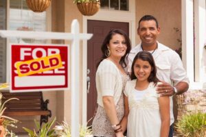 Family in Front of Their New Home with Sold Sign