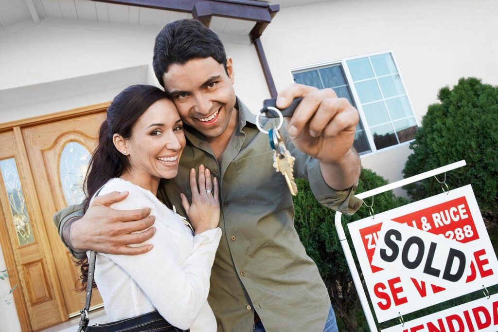 happy couple holding keys in front of their house